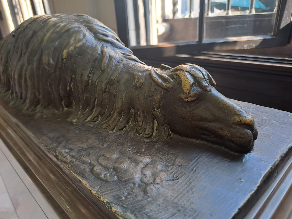 Der Bronzeguss eines Lamas, dass auf dem Boden liegt und schläft.