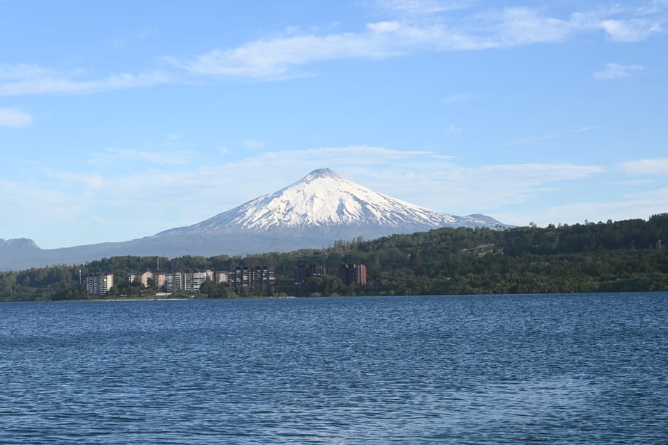 Sicht auf den aktiven Vulkan bei Villarrica mit See im Vordergrund bei schönem Wetter, die Bergspitze ist dabei mit Schnee bedeckt