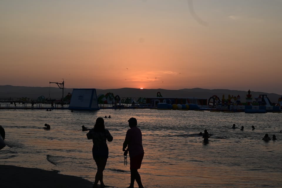 Strand bei Abendsonne, im Hintergrund ist eine schwimmende Kinderhüpfburg zu sehen.