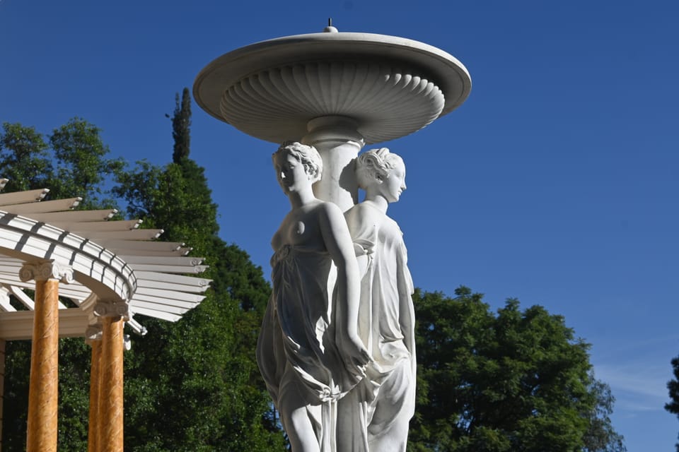 Ein Springbrunnen im Park der von zwei halbnackten marmornen Frauen am Kopf getragen wird.